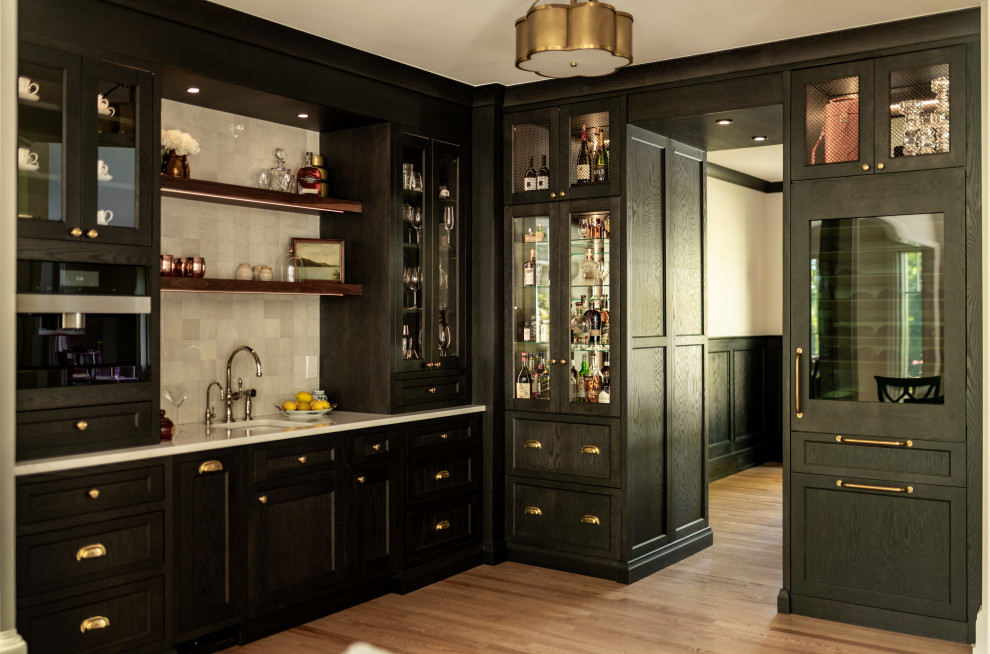 Wet bar - mid-sized transitional l-shaped light wood floor and brown floor wet bar idea in Detroit with shaker cabinets, white backsplash, black appliances, an island, an undermount sink, black cabinets, quartz countertops, stone tile backsplash and white countertops