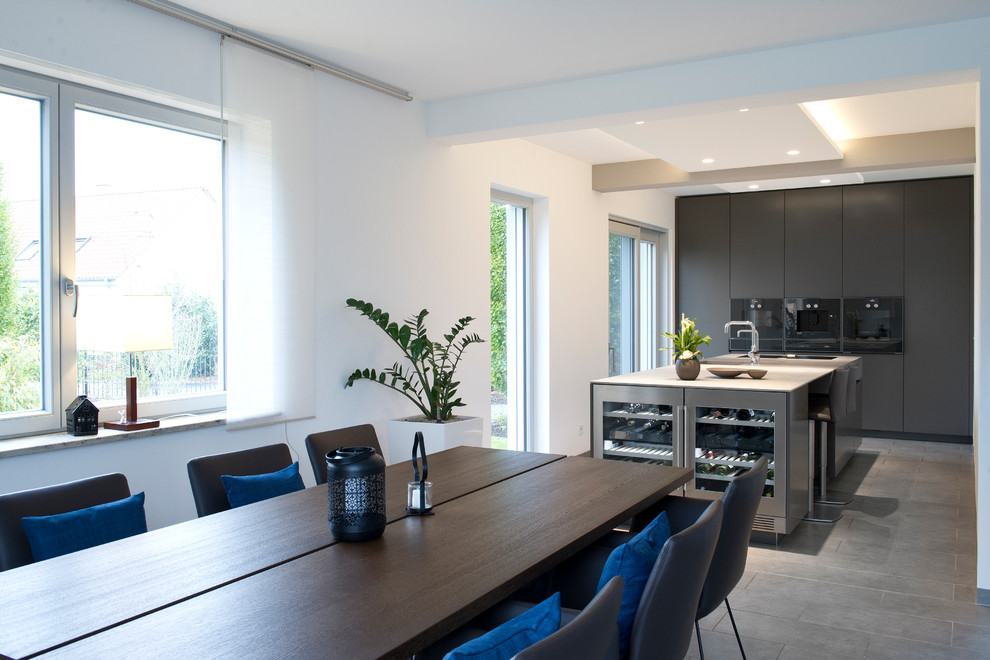 This is an example of a large contemporary galley open plan kitchen in Other with an integrated sink, flat-panel cabinets, grey cabinets, stainless steel benchtops, black appliances, cement tiles, with island, grey floor and beige benchtop.