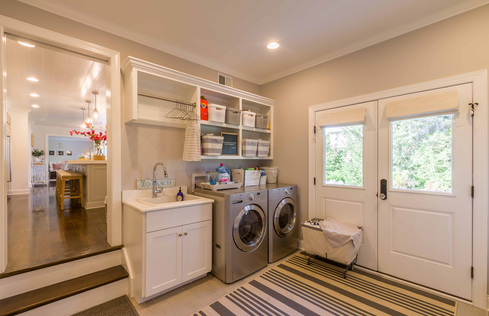 This is an example of a mid-sized traditional galley dedicated laundry room in Chicago with shaker cabinets, white cabinets, solid surface benchtops, white walls, ceramic floors, a side-by-side washer and dryer, grey floor, a drop-in sink, white benchtop, beige splashback, cement tile splashback, wallpaper and wallpaper.