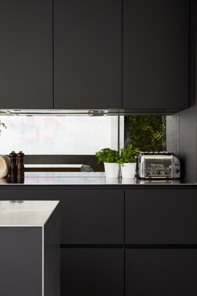This is an example of a small modern single-wall eat-in kitchen in London with flat-panel cabinets, black cabinets, stainless steel benchtops and with island.