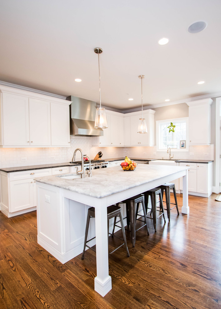 Photo of a large transitional l-shaped open plan kitchen in Philadelphia with a farmhouse sink, recessed-panel cabinets, white cabinets, granite benchtops, white splashback, subway tile splashback, stainless steel appliances, dark hardwood floors and with island.