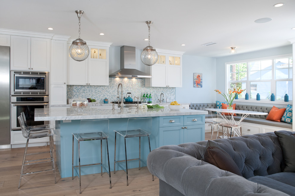 Inspiration for a large beach style l-shaped eat-in kitchen in Los Angeles with a farmhouse sink, shaker cabinets, white cabinets, blue splashback, mosaic tile splashback, stainless steel appliances, medium hardwood floors, with island and marble benchtops.
