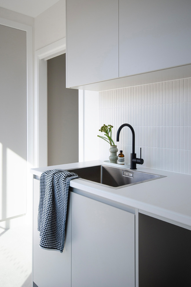 Idéer för mellanstora funkis linjära vitt tvättstugor enbart för tvätt, med en enkel diskho, laminatbänkskiva, vitt stänkskydd, stänkskydd i mosaik, vita väggar, klinkergolv i porslin, en tvättmaskin och torktumlare bredvid varandra och grått golv