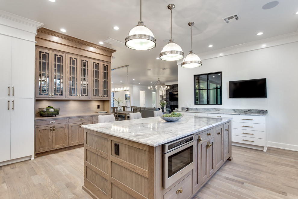 This is an example of an expansive transitional open plan kitchen in Oklahoma City with a farmhouse sink, flat-panel cabinets, white cabinets, white splashback, subway tile splashback, stainless steel appliances, medium hardwood floors, with island, multi-coloured benchtop and marble benchtops.