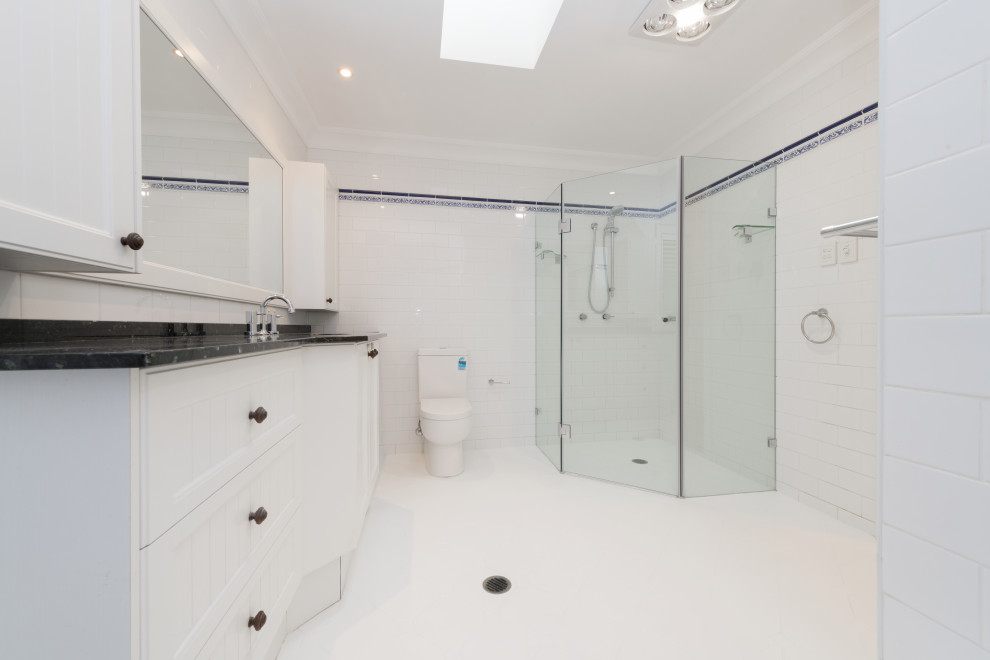 Small traditional bathroom in Sydney with white cabinets, a corner shower, a two-piece toilet, solid surface benchtops, a hinged shower door, a single vanity, a freestanding vanity, recessed-panel cabinets, a corner tub, white tile, ceramic tile, white walls, ceramic floors, with a sauna, an undermount sink, white floor and black benchtops.