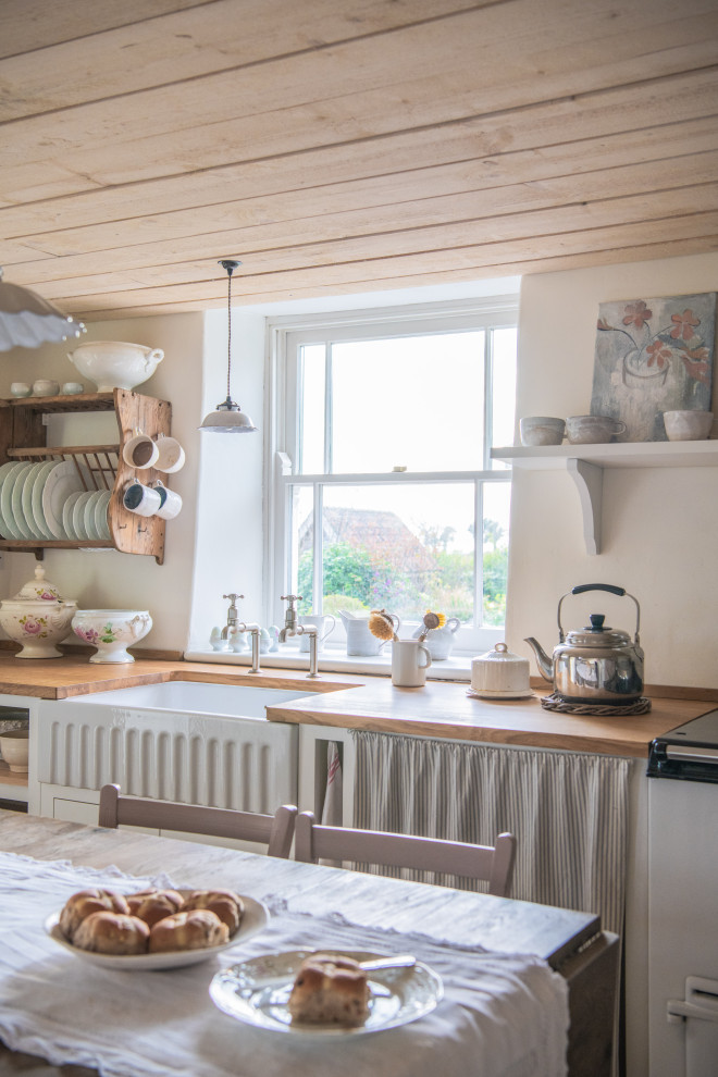 This is an example of a small shabby-chic style single-wall kitchen/diner in London with a belfast sink, shaker cabinets, white cabinets, wood worktops, white appliances, no island, beige floors, brown worktops and a timber clad ceiling.