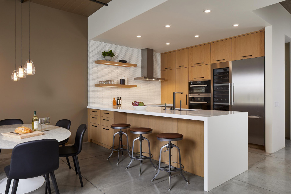 Inspiration for a contemporary u-shaped kitchen in San Francisco with an undermount sink, flat-panel cabinets, medium wood cabinets, white splashback, mosaic tile splashback, stainless steel appliances, concrete floors, a peninsula, grey floor and white benchtop.