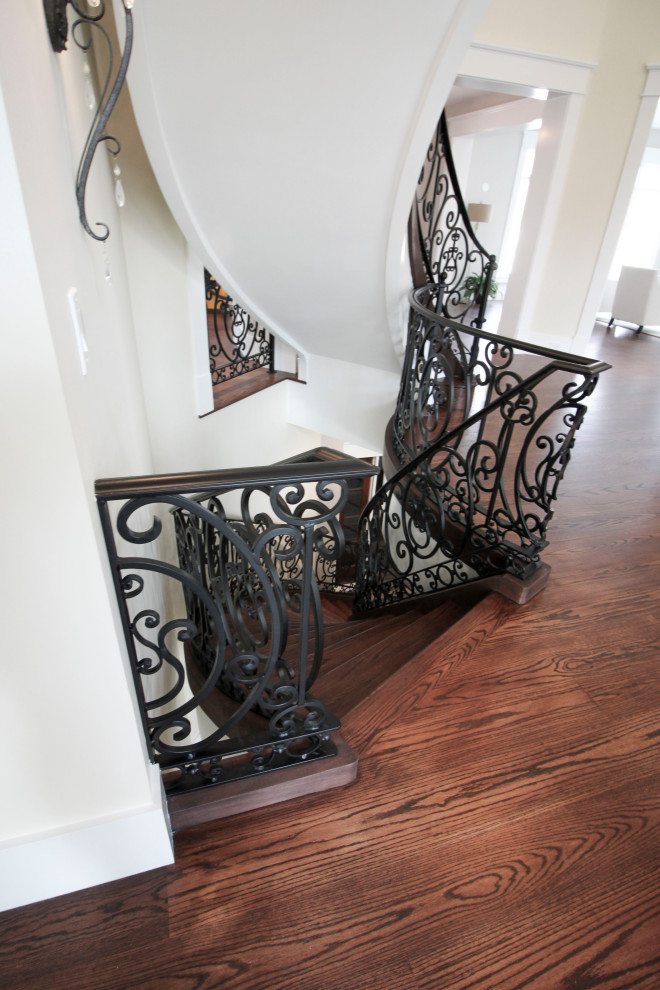 This is an example of an expansive transitional wood curved staircase in DC Metro with wood risers and metal railing.