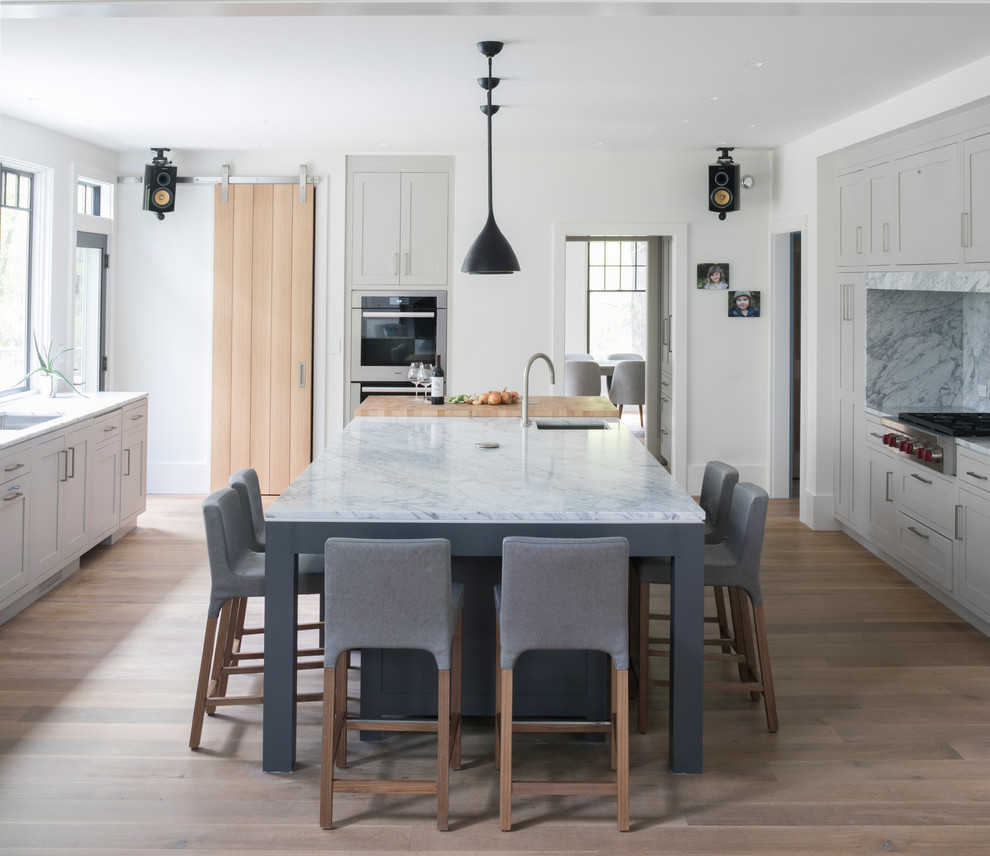 Country eat-in kitchen in New York with an undermount sink, shaker cabinets, grey cabinets, grey splashback, panelled appliances, light hardwood floors, with island and beige floor.