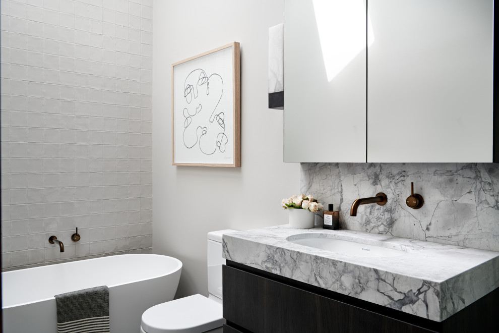 Photo of a small transitional master bathroom in Sydney with a freestanding tub, a one-piece toilet, ceramic tile, an undermount sink, marble benchtops, grey benchtops, a single vanity, a floating vanity, flat-panel cabinets, black cabinets, gray tile and grey walls.
