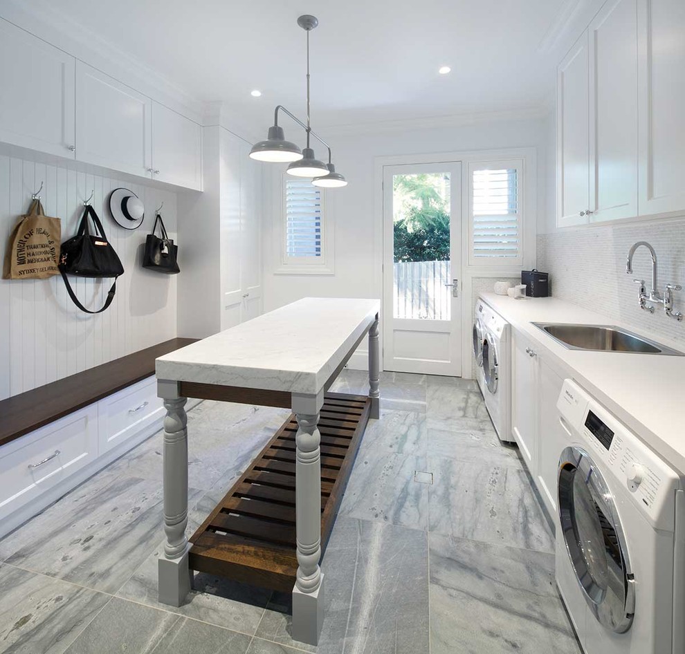 This is an example of an expansive traditional galley dedicated laundry room in Sydney with a single-bowl sink, shaker cabinets, white cabinets, solid surface benchtops, white walls, a side-by-side washer and dryer and grey floor.