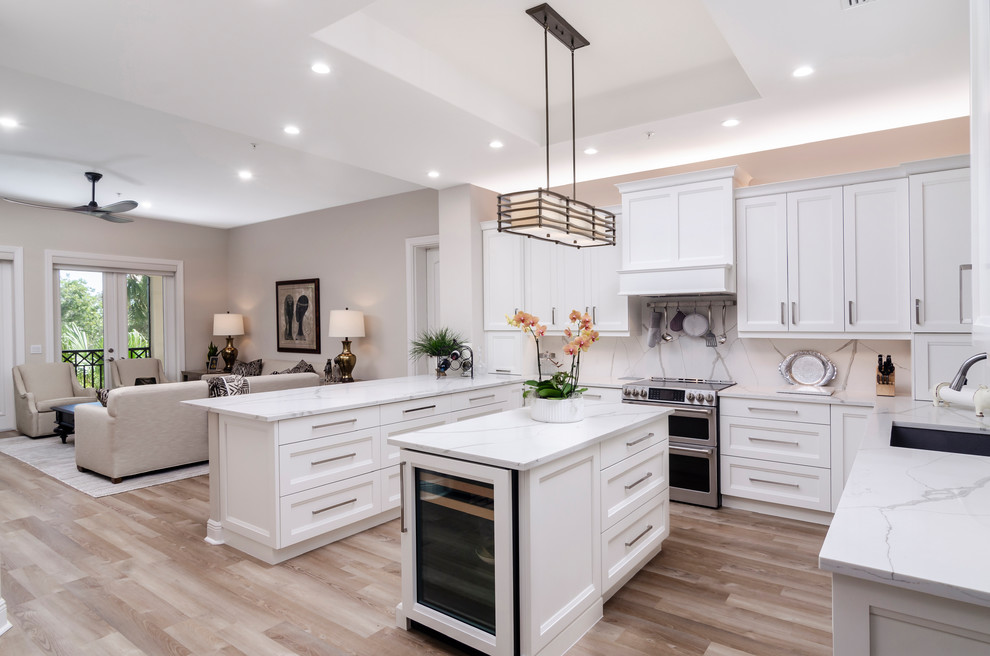 Inspiration for a mid-sized transitional u-shaped light wood floor and brown floor open concept kitchen remodel with an undermount sink, shaker cabinets, white cabinets, quartz countertops, white backsplash, stone slab backsplash, stainless steel appliances, an island and white countertops
