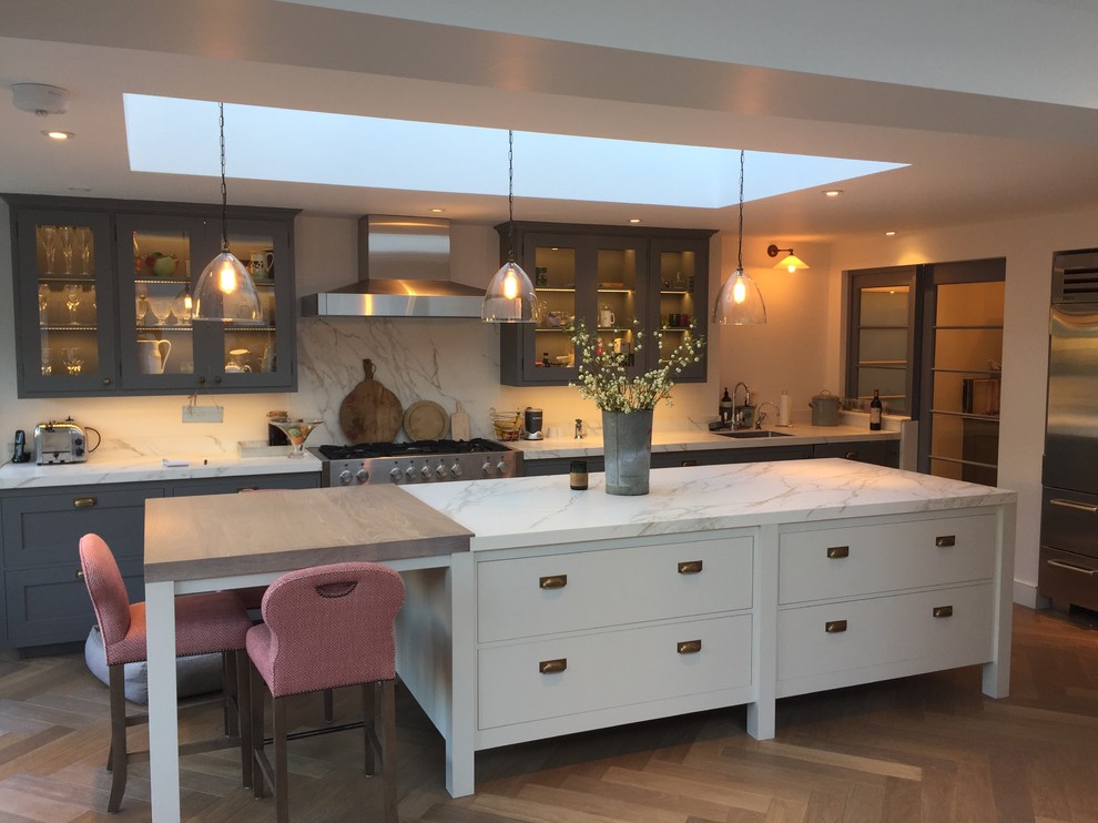 This is an example of a transitional single-wall kitchen in London with an undermount sink, flat-panel cabinets, marble benchtops, white splashback, marble splashback, stainless steel appliances, dark hardwood floors, with island, brown floor and white benchtop.
