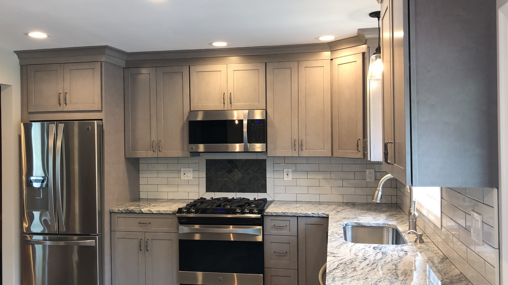Photo of a mid-sized modern l-shaped eat-in kitchen in New York with an undermount sink, shaker cabinets, grey cabinets, granite benchtops, grey splashback, glass tile splashback, stainless steel appliances, porcelain floors, with island, grey floor and grey benchtop.