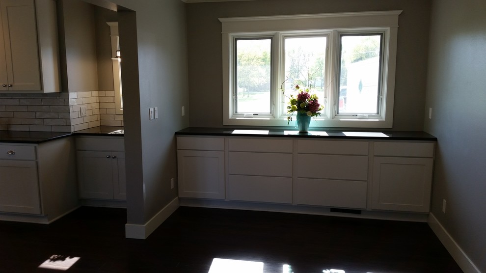 Example of a transitional galley dark wood floor eat-in kitchen design with white cabinets, granite countertops, white backsplash, subway tile backsplash and stainless steel appliances