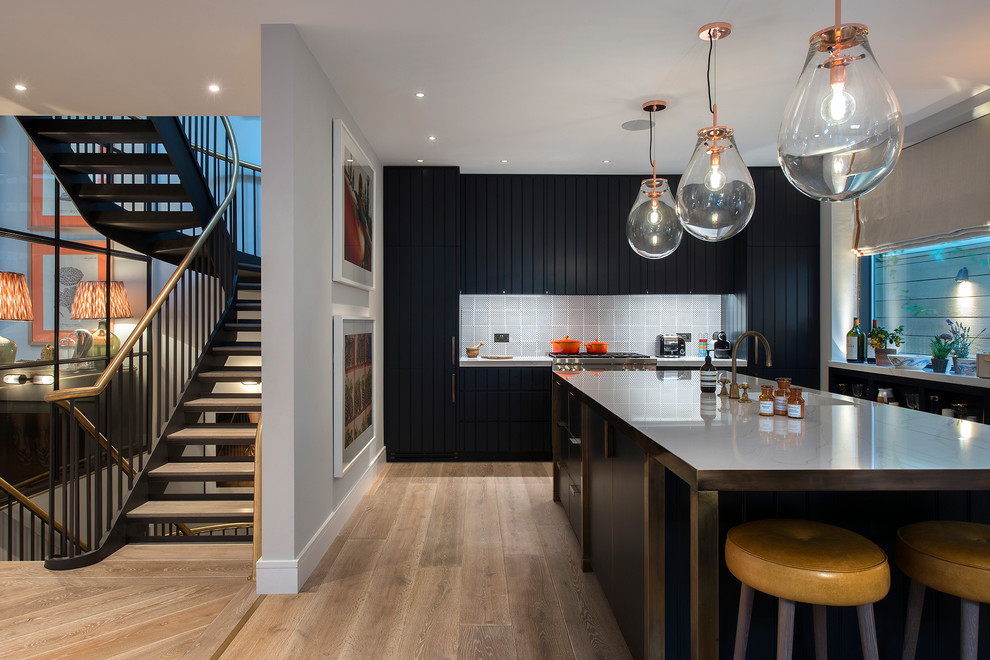 Photo of a modern l-shaped kitchen in London with light hardwood floors, with island, beige floor, flat-panel cabinets, black cabinets, stainless steel benchtops, grey splashback, ceramic splashback, panelled appliances and grey benchtop.
