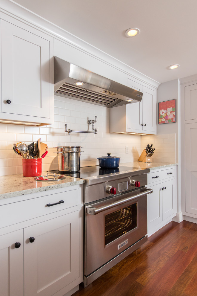 This is an example of a beach style eat-in kitchen in Providence with an undermount sink, shaker cabinets, white cabinets, granite benchtops, white splashback, medium hardwood floors and with island.