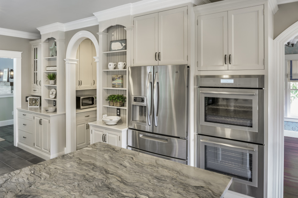 This is an example of a large beach style eat-in kitchen in Providence with a double-bowl sink, raised-panel cabinets, white cabinets, quartzite benchtops, white splashback, ceramic splashback, stainless steel appliances, ceramic floors, a peninsula, grey floor and multi-coloured benchtop.