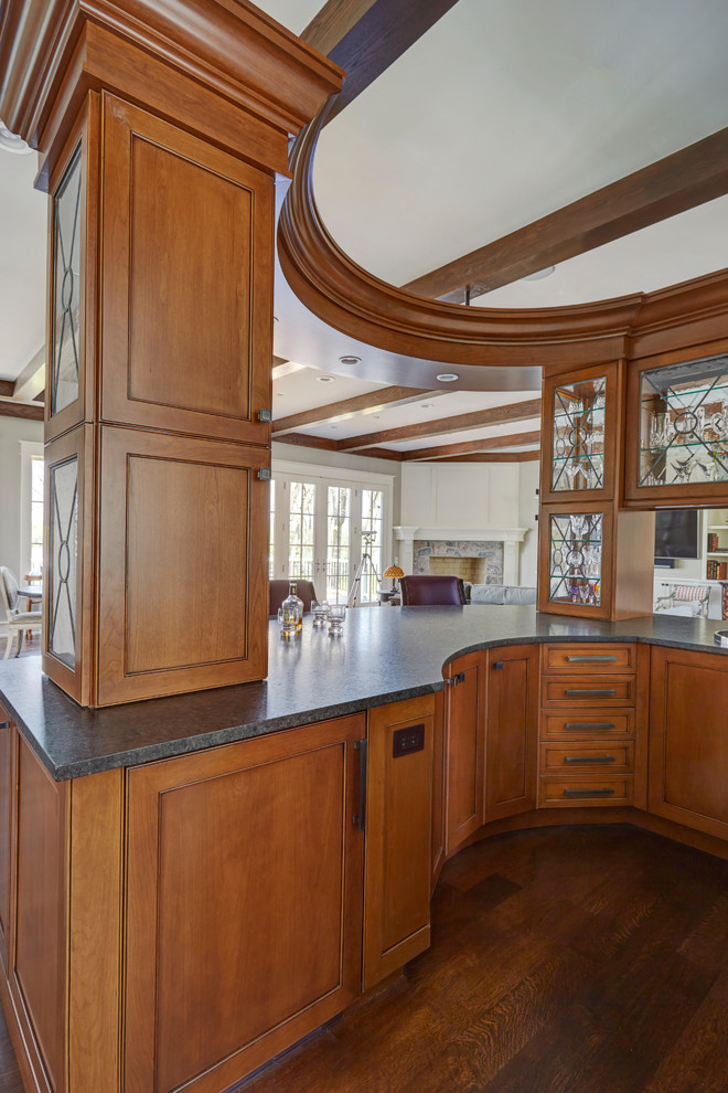 Inspiration for a large traditional galley wet bar in Chicago with a drop-in sink, medium wood cabinets, granite benchtops, dark hardwood floors, brown floor and black benchtop.