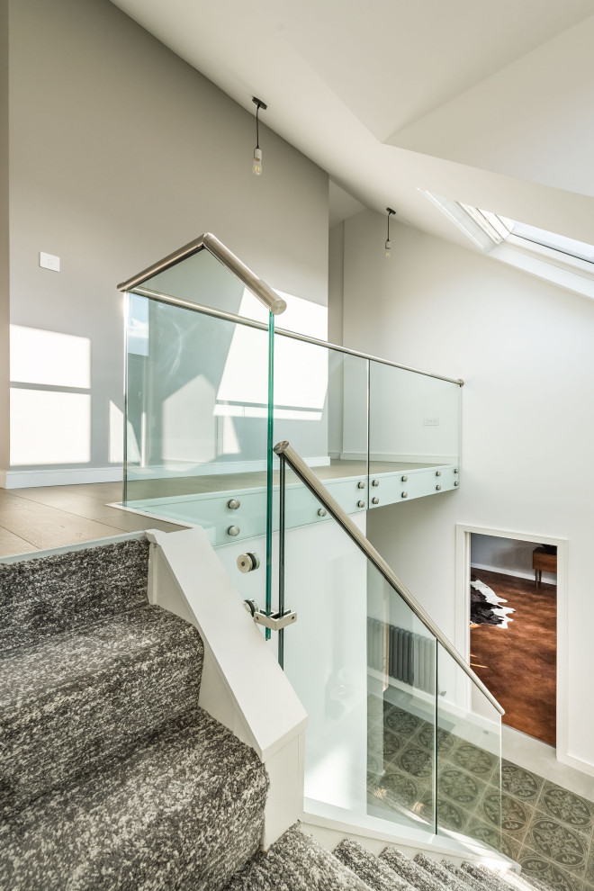 Example of a large trendy carpeted l-shaped glass railing staircase design in Essex with carpeted risers