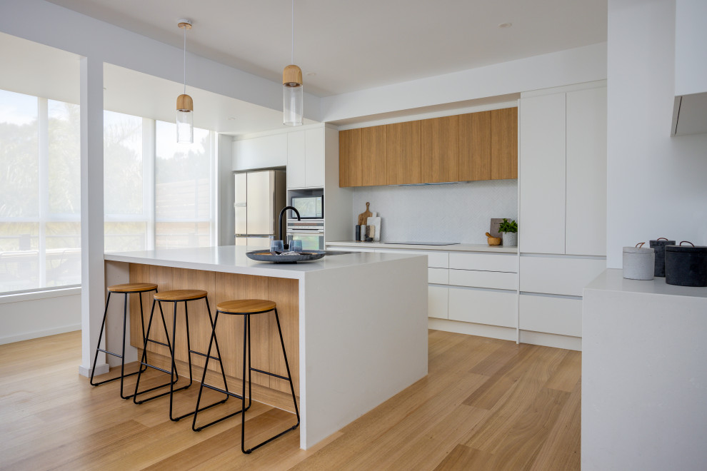 Inspiration for a large scandinavian u-shaped kitchen pantry in Melbourne with an undermount sink, recessed-panel cabinets, white cabinets, quartz benchtops, grey splashback, porcelain splashback, stainless steel appliances, medium hardwood floors, with island and white benchtop.