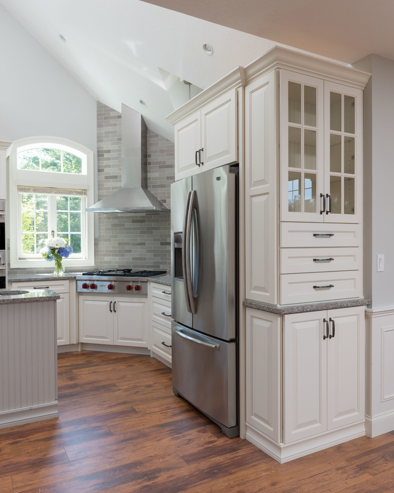 Photo of a contemporary u-shaped eat-in kitchen in Manchester with a drop-in sink, beaded inset cabinets, white cabinets, granite benchtops, grey splashback, stainless steel appliances, medium hardwood floors and with island.