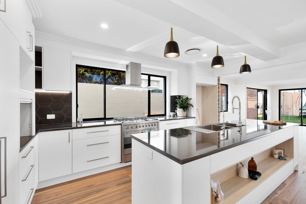 Design ideas for a mid-sized modern l-shaped open plan kitchen in Brisbane with a double-bowl sink, white cabinets, laminate benchtops, window splashback, stainless steel appliances, medium hardwood floors, with island, multi-coloured floor and black benchtop.