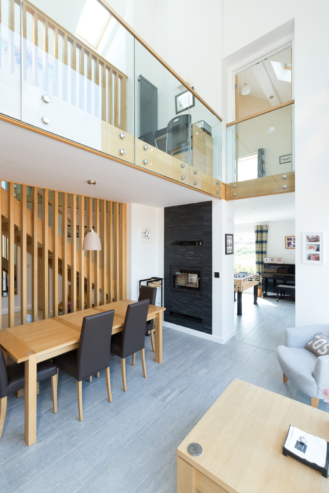 This is an example of a modern open plan dining in West Midlands with white walls, a ribbon fireplace, a metal fireplace surround and grey floor.