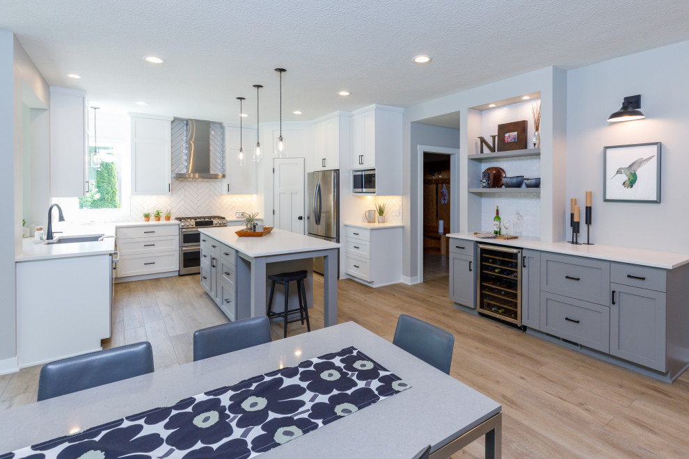 Mid-sized transitional u-shaped open plan kitchen in Minneapolis with an undermount sink, recessed-panel cabinets, white cabinets, quartz benchtops, white splashback, ceramic splashback, stainless steel appliances, vinyl floors, white benchtop and with island.
