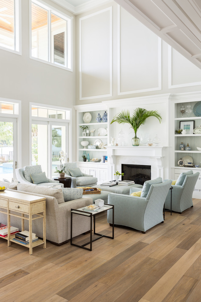 This is an example of a large beach style living room in Miami with white walls, light hardwood floors, a standard fireplace and a stone fireplace surround.