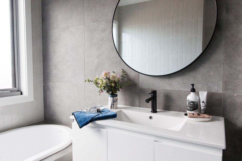 Design ideas for a mid-sized modern 3/4 bathroom in Canberra - Queanbeyan with furniture-like cabinets, white cabinets, a drop-in tub, gray tile, grey walls, an undermount sink, grey floor, a one-piece toilet, porcelain tile and porcelain floors.