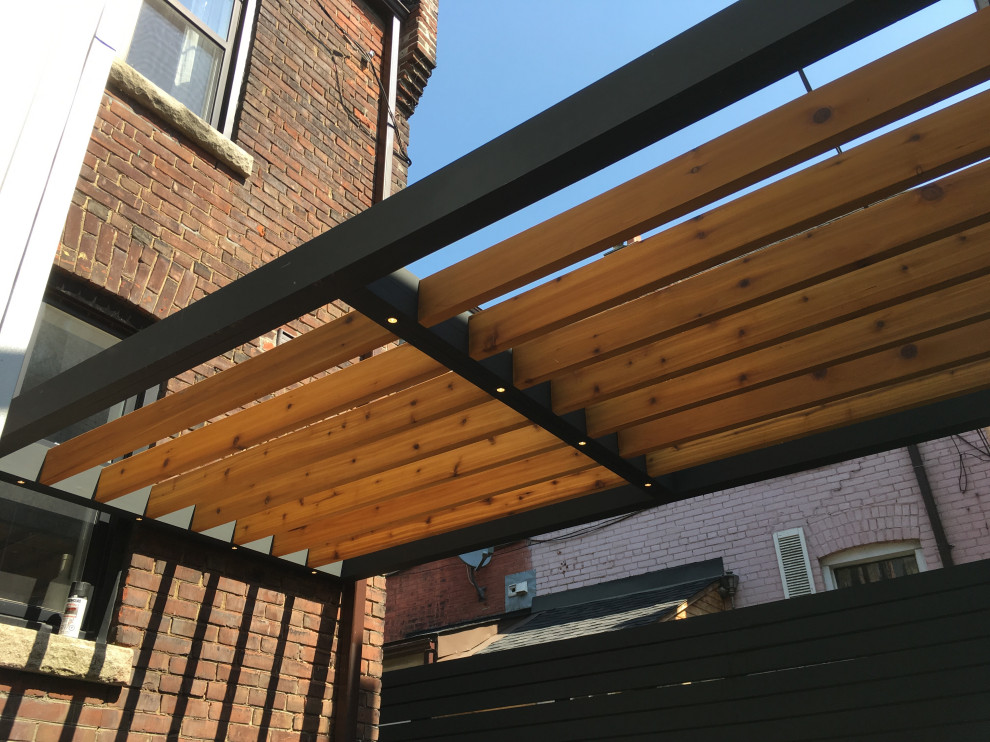 Photo of a mid-sized industrial backyard deck in Toronto with a pergola.