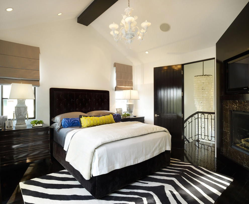 Mediterranean bedroom in Los Angeles with white walls, a corner fireplace, a stone fireplace surround and black floor.