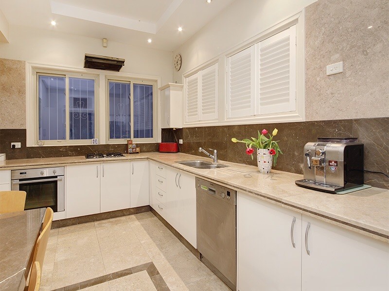 This is an example of a mid-sized contemporary l-shaped separate kitchen in Brisbane with white cabinets, limestone benchtops, grey splashback, limestone splashback, limestone floors, no island, pink floor and beige benchtop.