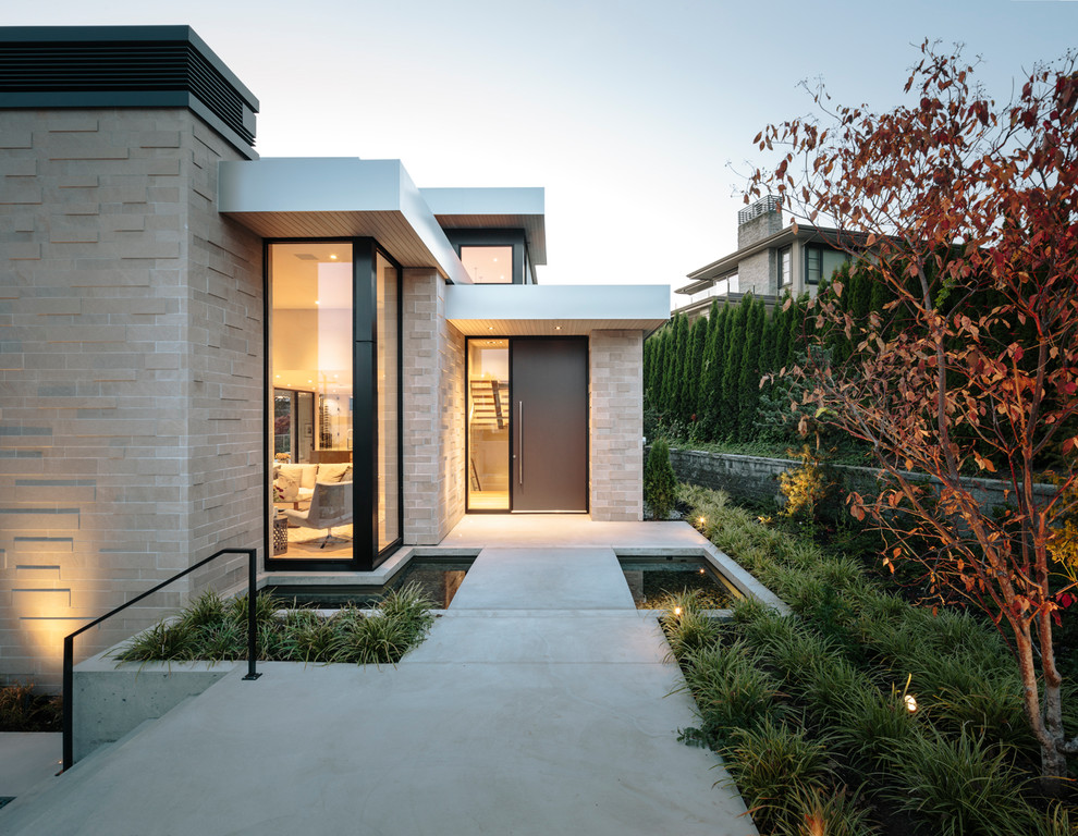 This is an example of a large contemporary three-storey beige house exterior in Vancouver with stone veneer and a flat roof.