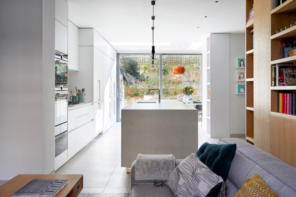 Photo of a large traditional galley open plan kitchen in London with an integrated sink, flat-panel cabinets, white cabinets, marble benchtops, white splashback, marble splashback, panelled appliances, concrete floors, with island, grey floor and white benchtop.