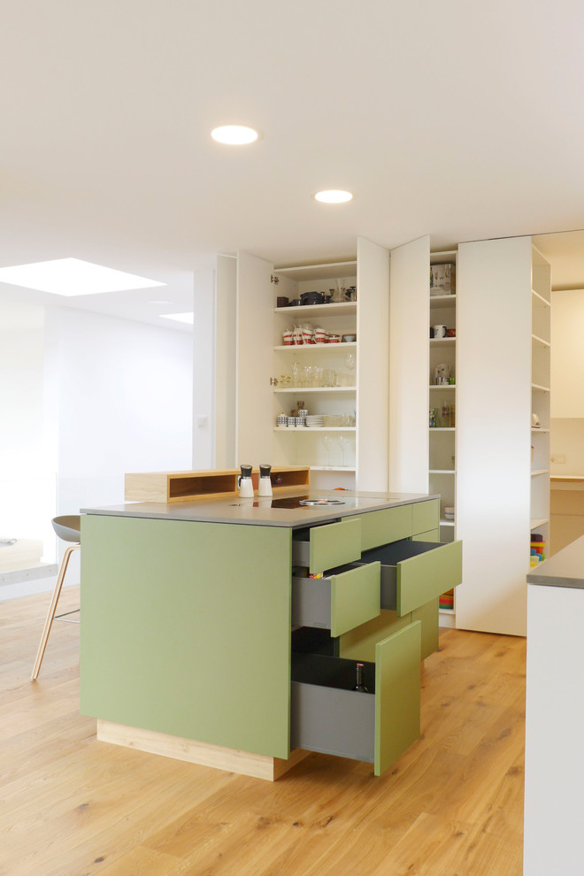 This is an example of a small scandinavian galley eat-in kitchen in Frankfurt with an undermount sink, flat-panel cabinets, green cabinets, quartz benchtops, white splashback, timber splashback, black appliances, medium hardwood floors, with island, brown floor and grey benchtop.