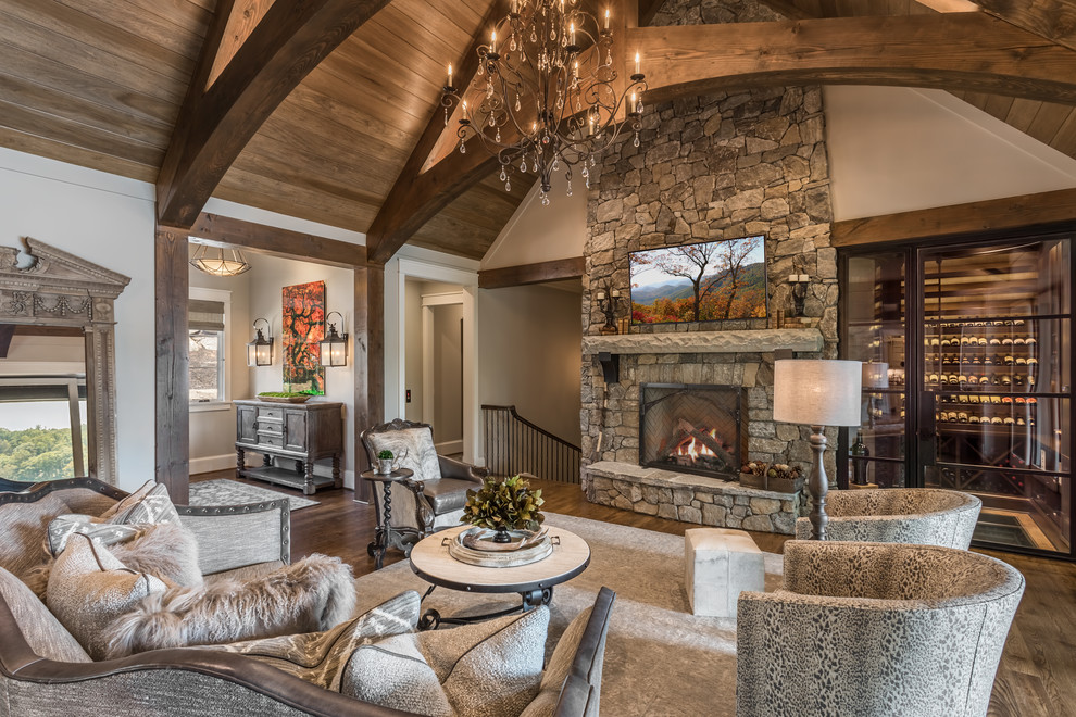 Photo of an expansive country open concept family room in Other with a standard fireplace, a stone fireplace surround, grey walls, dark hardwood floors and a wall-mounted tv.