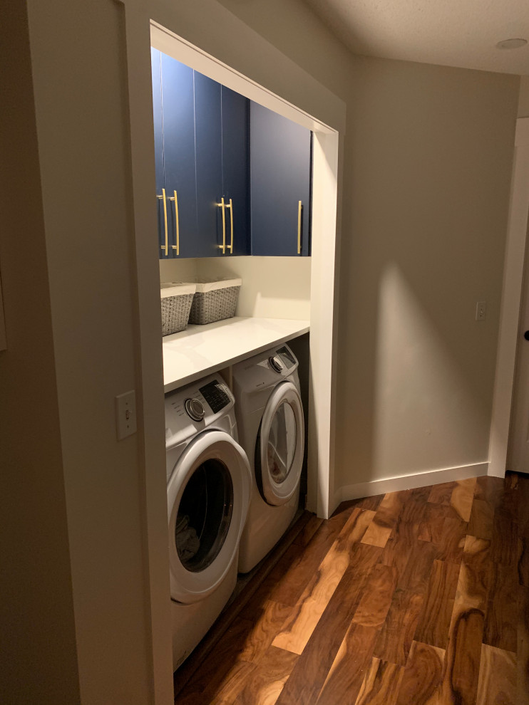 Immagine di una lavanderia minimalista con ante lisce, ante blu, top in quarzo composito, pareti grigie, pavimento in gres porcellanato, lavatrice e asciugatrice affiancate, pavimento grigio e top bianco
