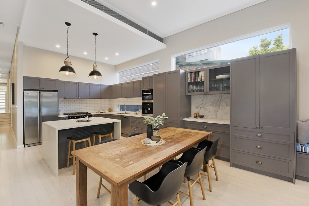 Design ideas for a large beach style l-shaped eat-in kitchen in Sydney with a double-bowl sink, recessed-panel cabinets, grey cabinets, marble benchtops, white splashback, ceramic splashback, stainless steel appliances, light hardwood floors, with island and white floor.