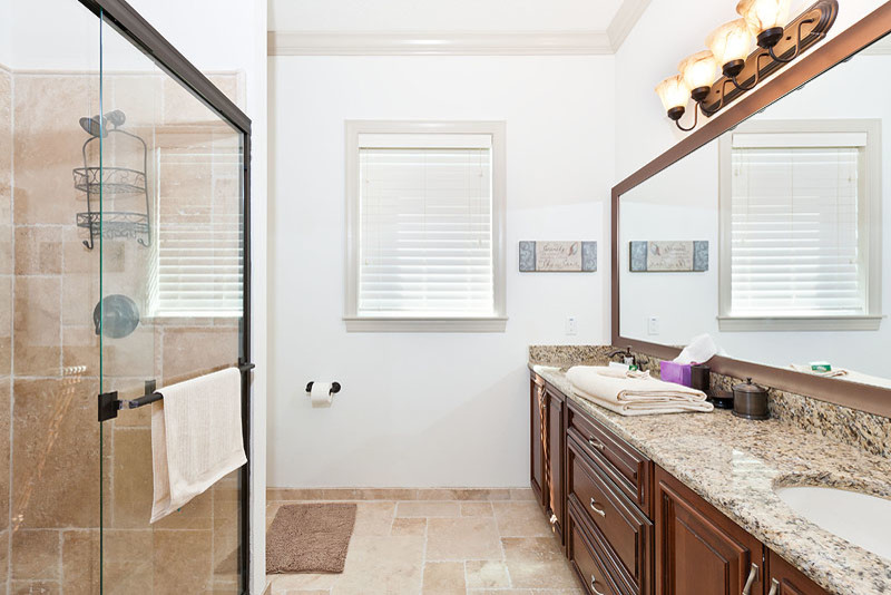 Design ideas for a large beach style master bathroom in Orlando with an undermount sink, raised-panel cabinets, dark wood cabinets, granite benchtops, an undermount tub, an open shower, a one-piece toilet, beige tile, stone tile, white walls and travertine floors.