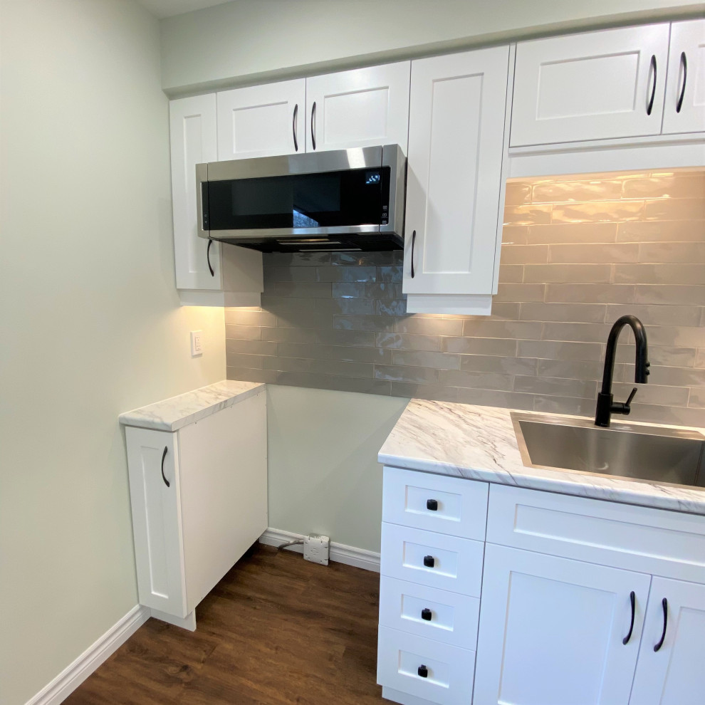 Inspiration for a mid-sized transitional galley vinyl floor eat-in kitchen remodel in Toronto with a drop-in sink, shaker cabinets, white cabinets, laminate countertops, gray backsplash and stainless steel appliances