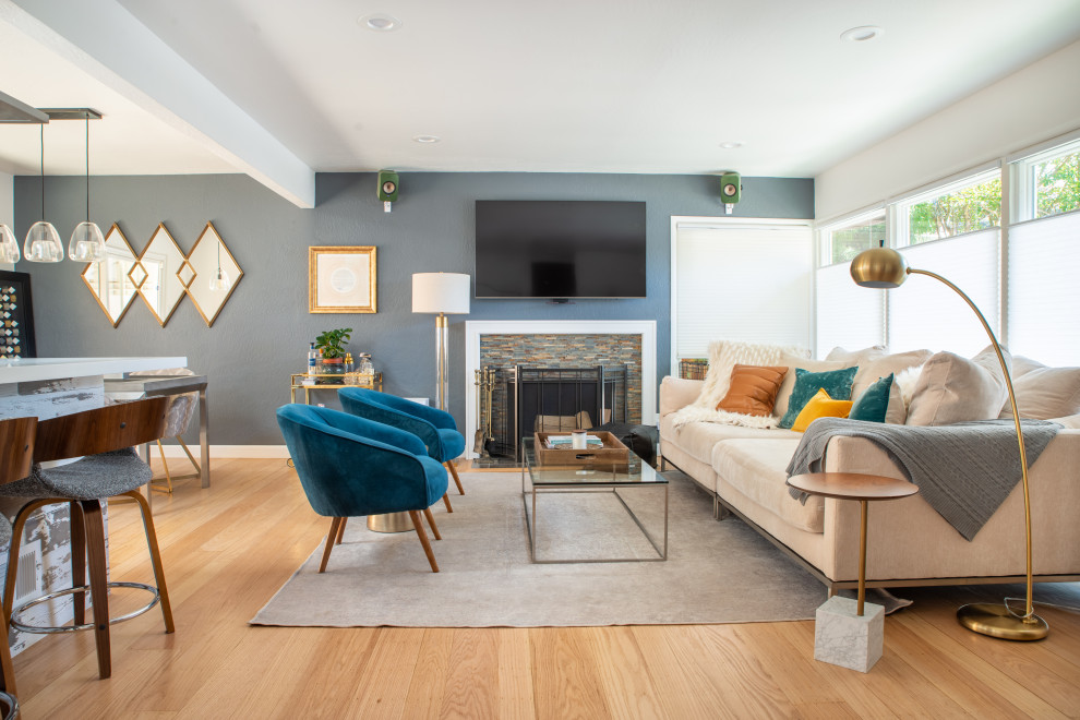 Example of a transitional open concept medium tone wood floor and brown floor living room design in San Francisco with blue walls, a standard fireplace, a stacked stone fireplace and a wall-mounted tv
