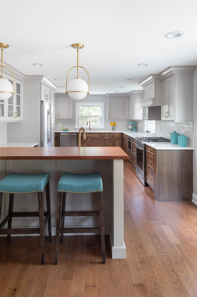 Example of a large transitional medium tone wood floor and brown floor kitchen design with an undermount sink, recessed-panel cabinets, medium tone wood cabinets, quartz countertops, white backsplash, subway tile backsplash, stainless steel appliances, a peninsula and white countertops