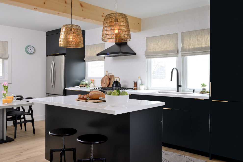 Photo of a mid-sized scandinavian single-wall eat-in kitchen in Toronto with a single-bowl sink, flat-panel cabinets, black cabinets, quartz benchtops, white splashback, ceramic splashback, stainless steel appliances, light hardwood floors, with island, beige floor, white benchtop and exposed beam.