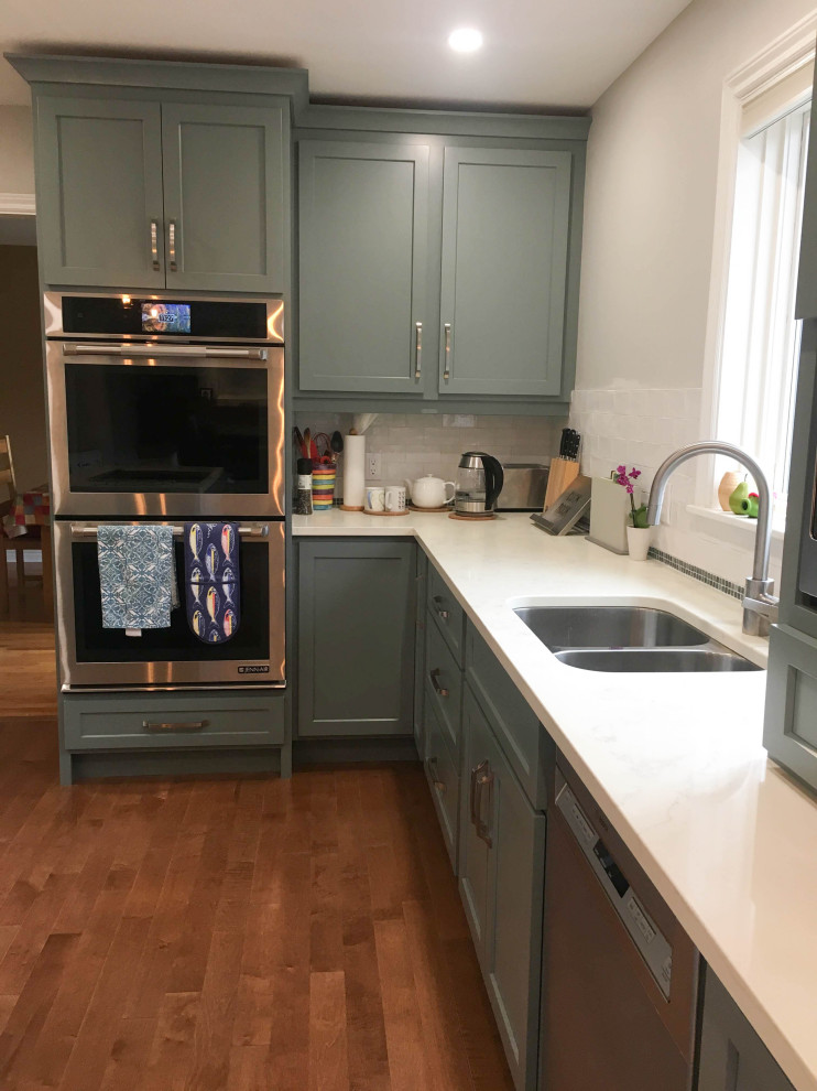 Example of a mid-sized transitional l-shaped medium tone wood floor and brown floor enclosed kitchen design with a double-bowl sink, shaker cabinets, gray cabinets, quartz countertops, white backsplash, porcelain backsplash, stainless steel appliances, an island and white countertops
