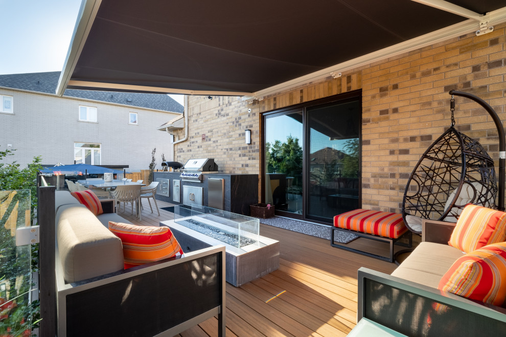 Outdoor kitchen deck - mid-sized transitional side yard second story glass railing outdoor kitchen deck idea in Toronto with an awning