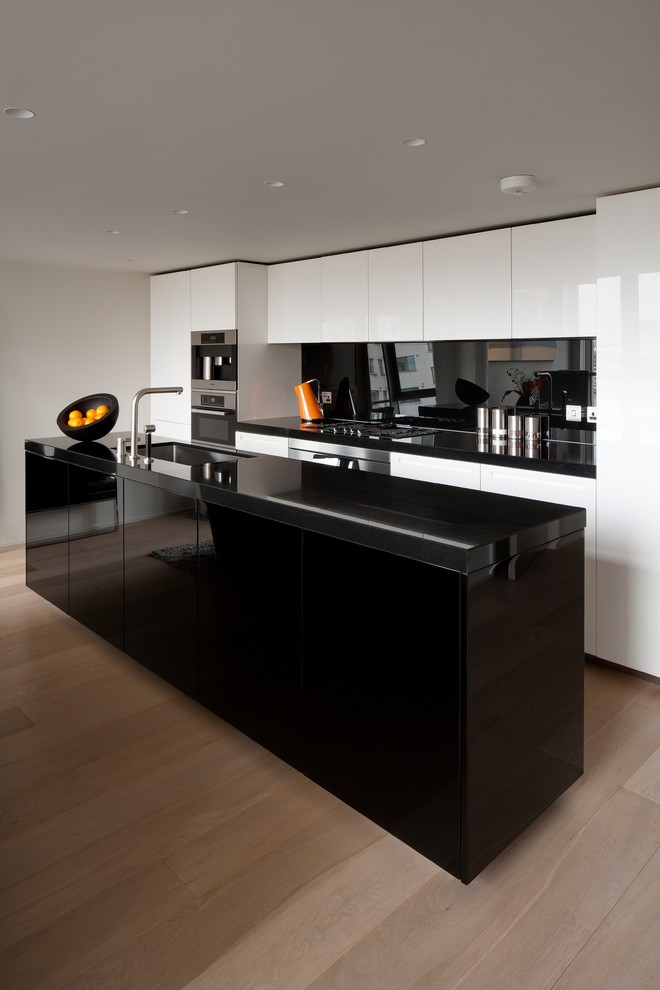 Contemporary galley kitchen in London with an undermount sink, flat-panel cabinets, black splashback, light hardwood floors and with island.