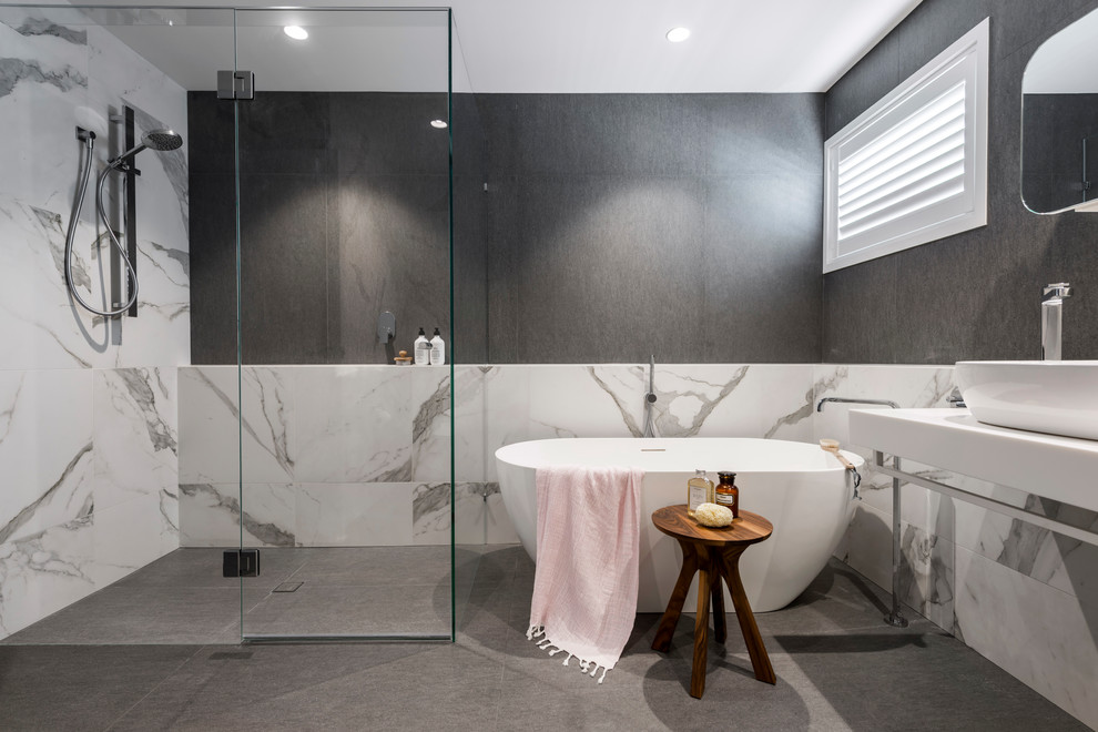 This is an example of a contemporary bathroom in Brisbane with a freestanding tub, a curbless shower, gray tile, white tile, grey walls, a vessel sink, grey floor, a hinged shower door and white benchtops.