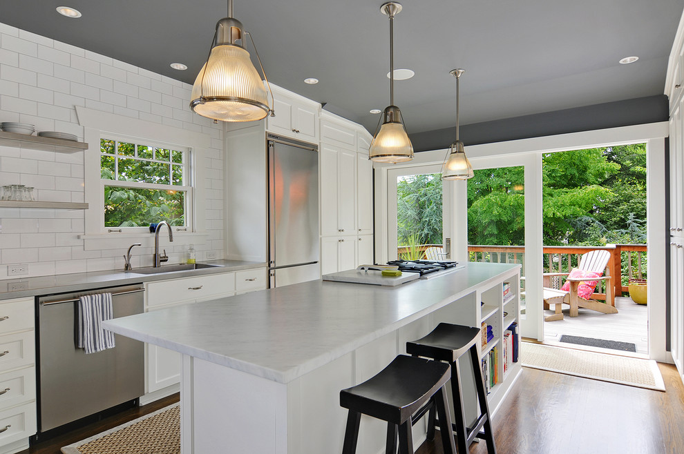 Transitional eat-in kitchen in Seattle with an undermount sink, recessed-panel cabinets, white cabinets, marble benchtops, white splashback, ceramic splashback, stainless steel appliances, medium hardwood floors, with island, brown floor and grey benchtop.